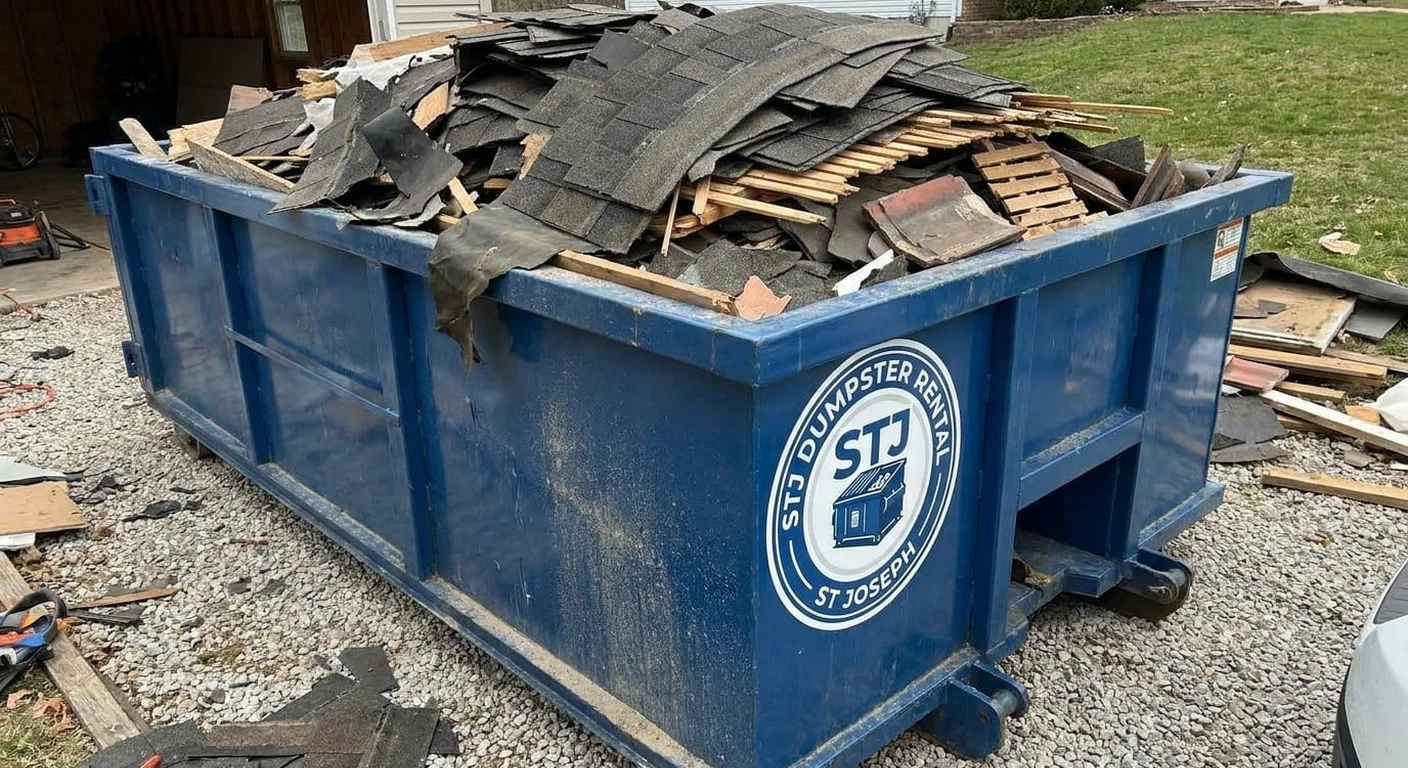 A STJ Dumpster Rental St Joseph dumpster filled with real roofing tear-off debris in front of a home